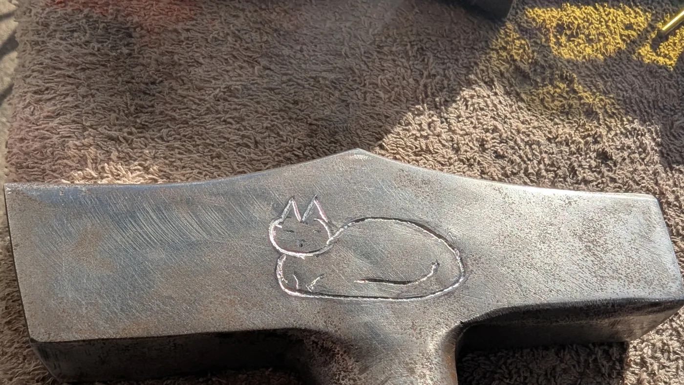 A small sleeping cat engraved in outline on a steel hammer-head handle
