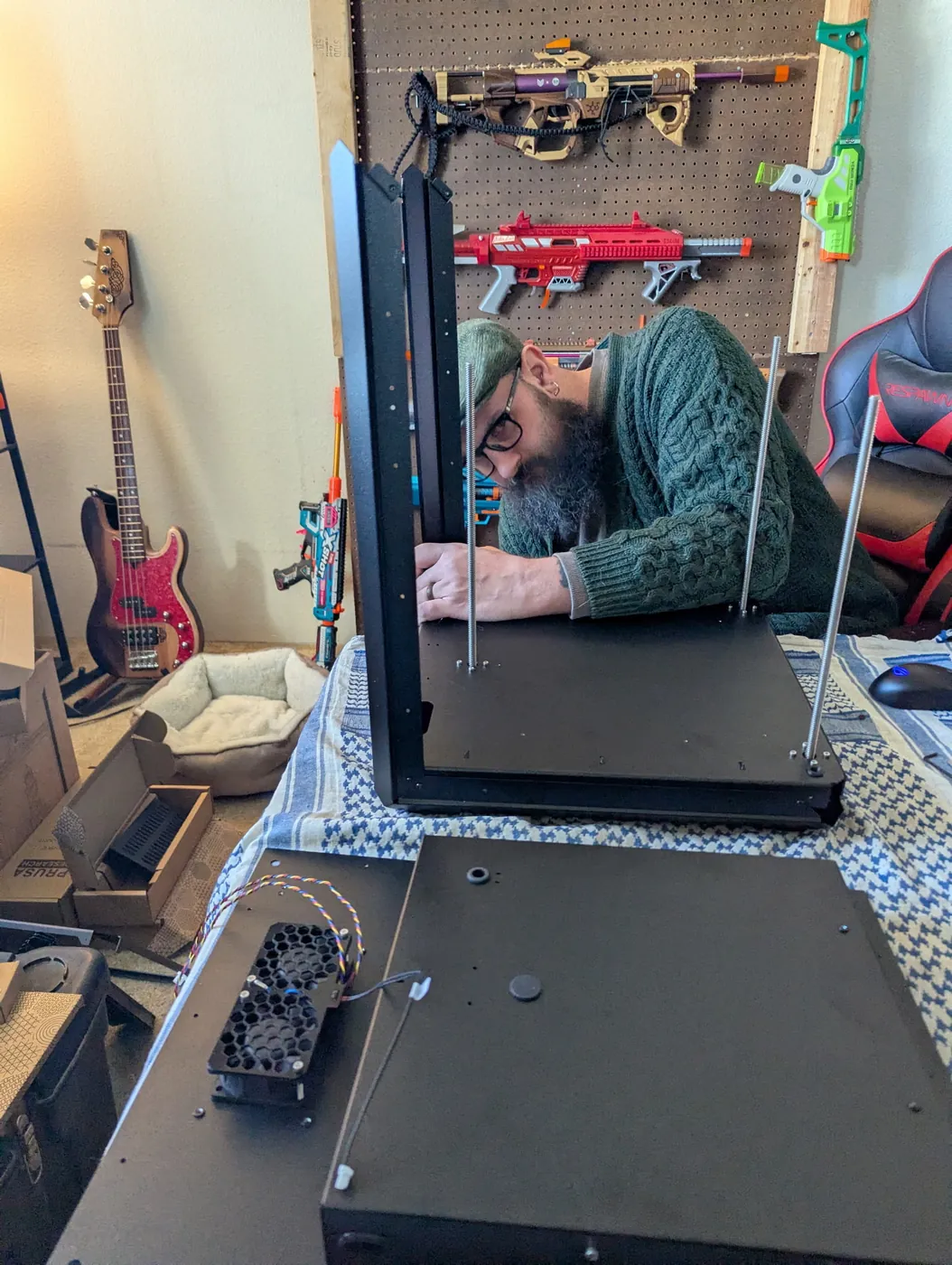 Tyler hunched over a computer case on an indoor bench, foam blasters hanging on the wall behind him
