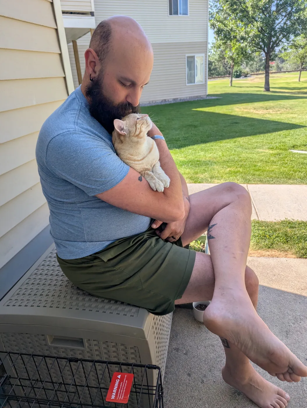 Tyler sitting on a patio storage bench, hugging Luca, an orange tabby, to his chest